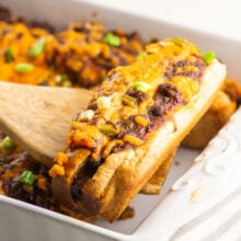 A vegan baked hot dog is held on a spatula over the rest of the casserole dish.
