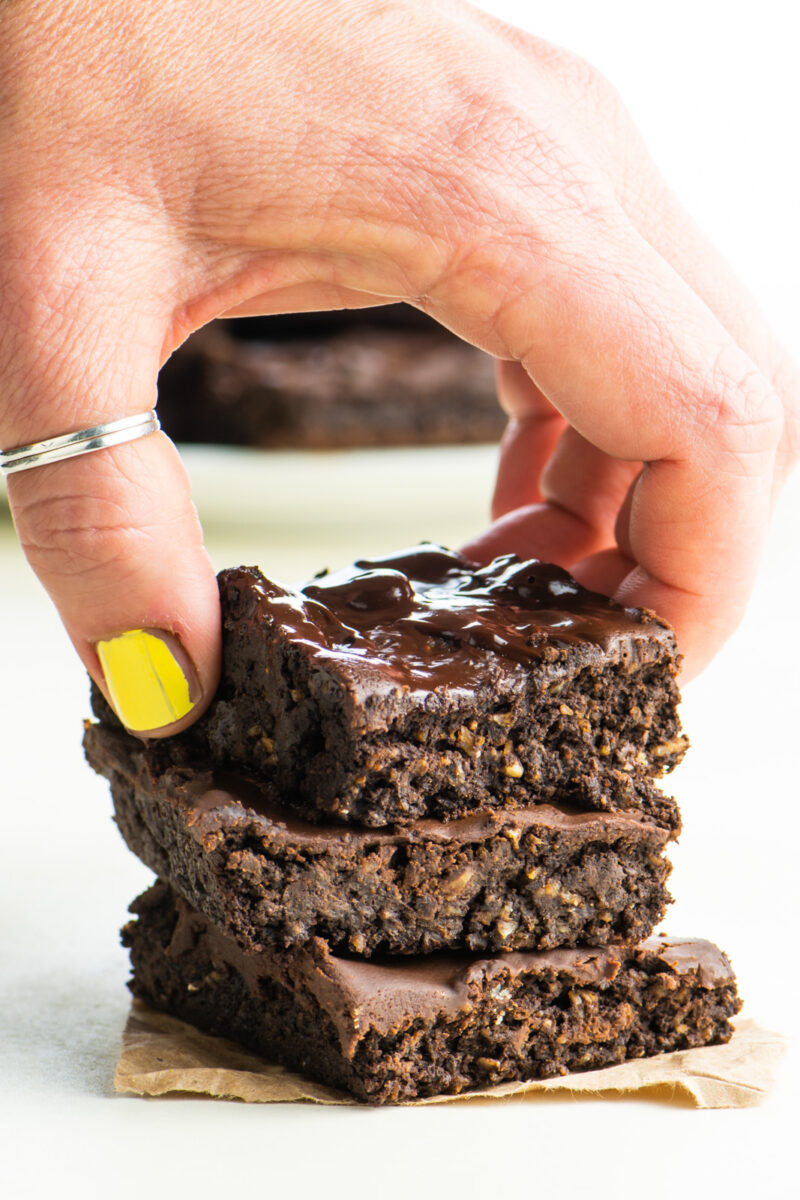 A hand reaches in and grabs the top brownie in a stack of three.