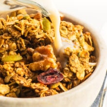 Granola with nuts and dried fruit, milk being poured over it in a bowl.