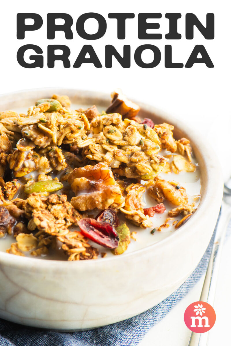 Bowl of protein granola mixed with nuts and dried fruits, set in milk on a textured napkin.