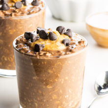 A glass full of chocolate peanut butter overnight oats topped with peanut butter and chocolate chips.