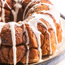 A loaf of Vegan Monkey Bread sits on a plate with lots of frosting drizzled over the top.
