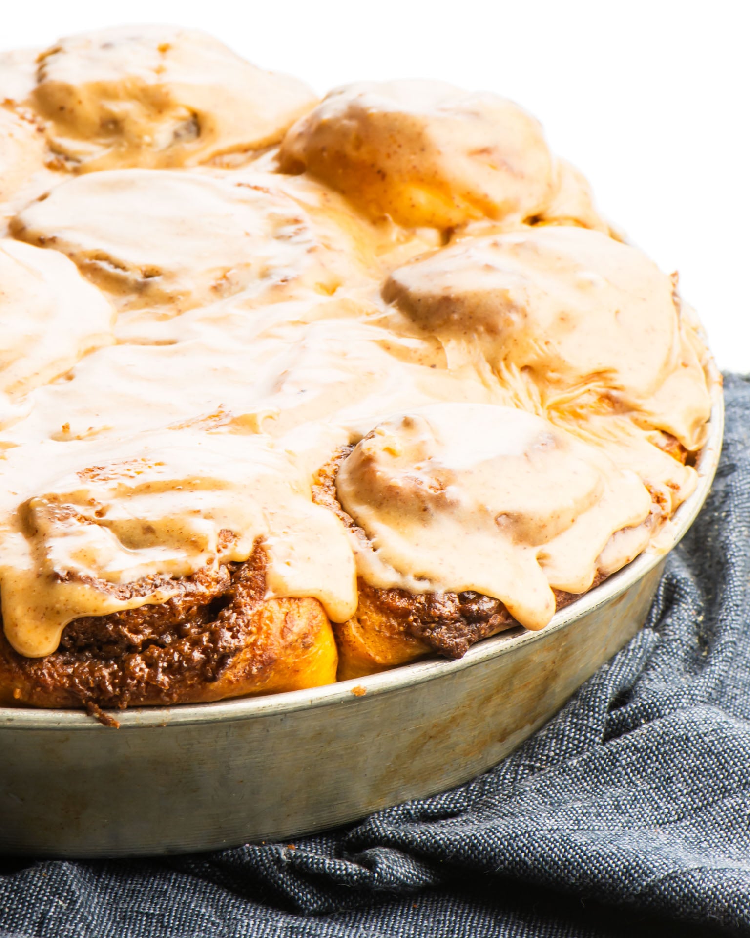 A batch of freshly baked and frosted cinnamon rolls in a pan sit on a dark blue kitchen towel.