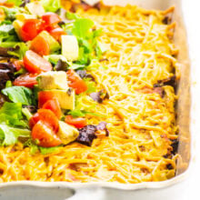 Vegan Mexican Lasagna in a casserole dish with chopped veggies on top.