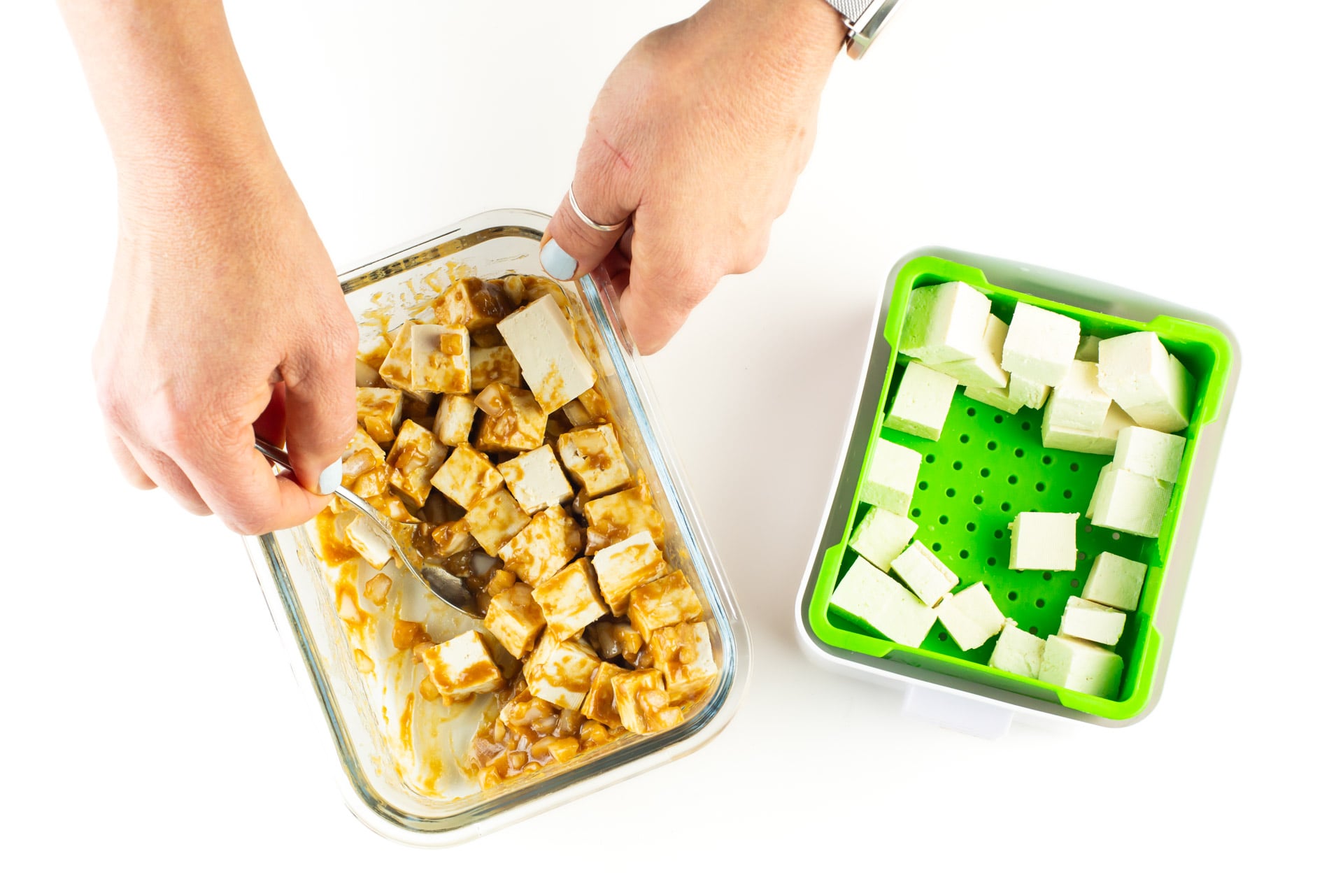 A hand uses a spoon to stir ingredients next to a green container.
