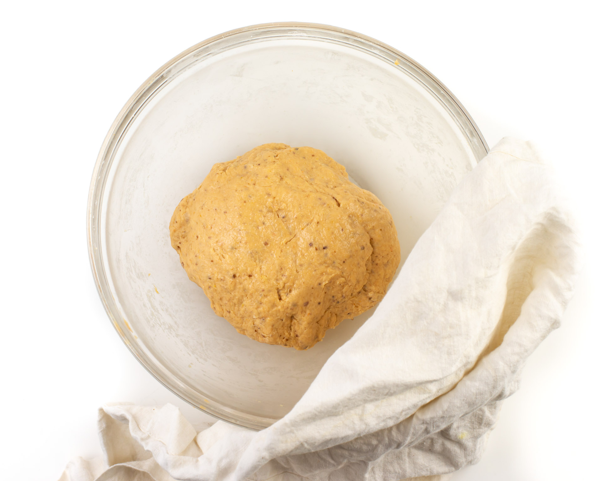 A ball of sweet potato dough is in a glass bowl with a kitchen towel beside it.