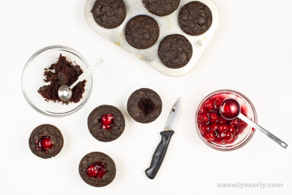 Looking down on cupcakes with holes in the middle and cherry pie filling spooned in.