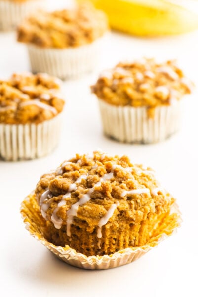 A vegan banana muffin with glaze on top with several more behind it.