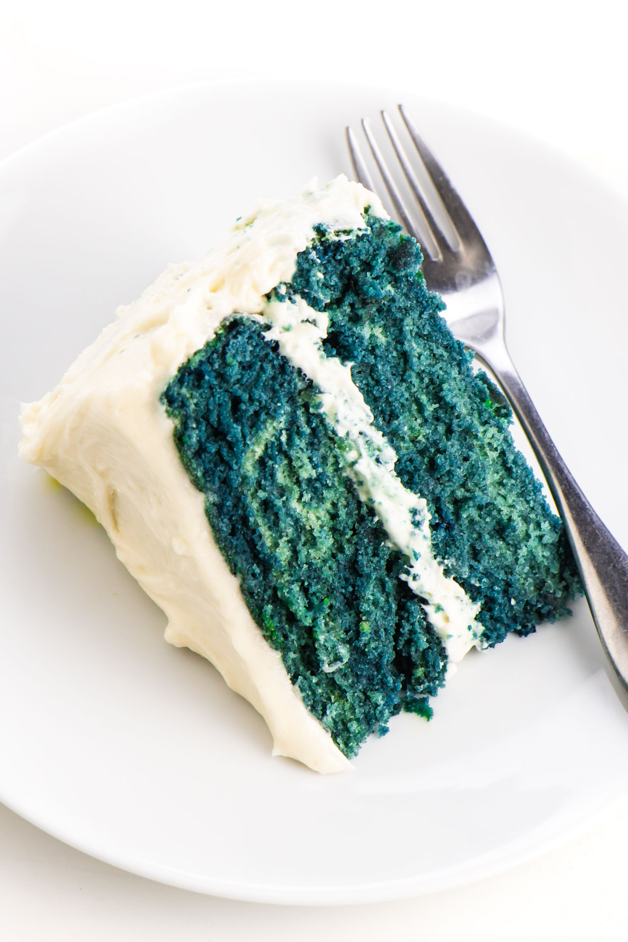 A slice of blue velvet cake lays on its side on a plate with a fork next to it.