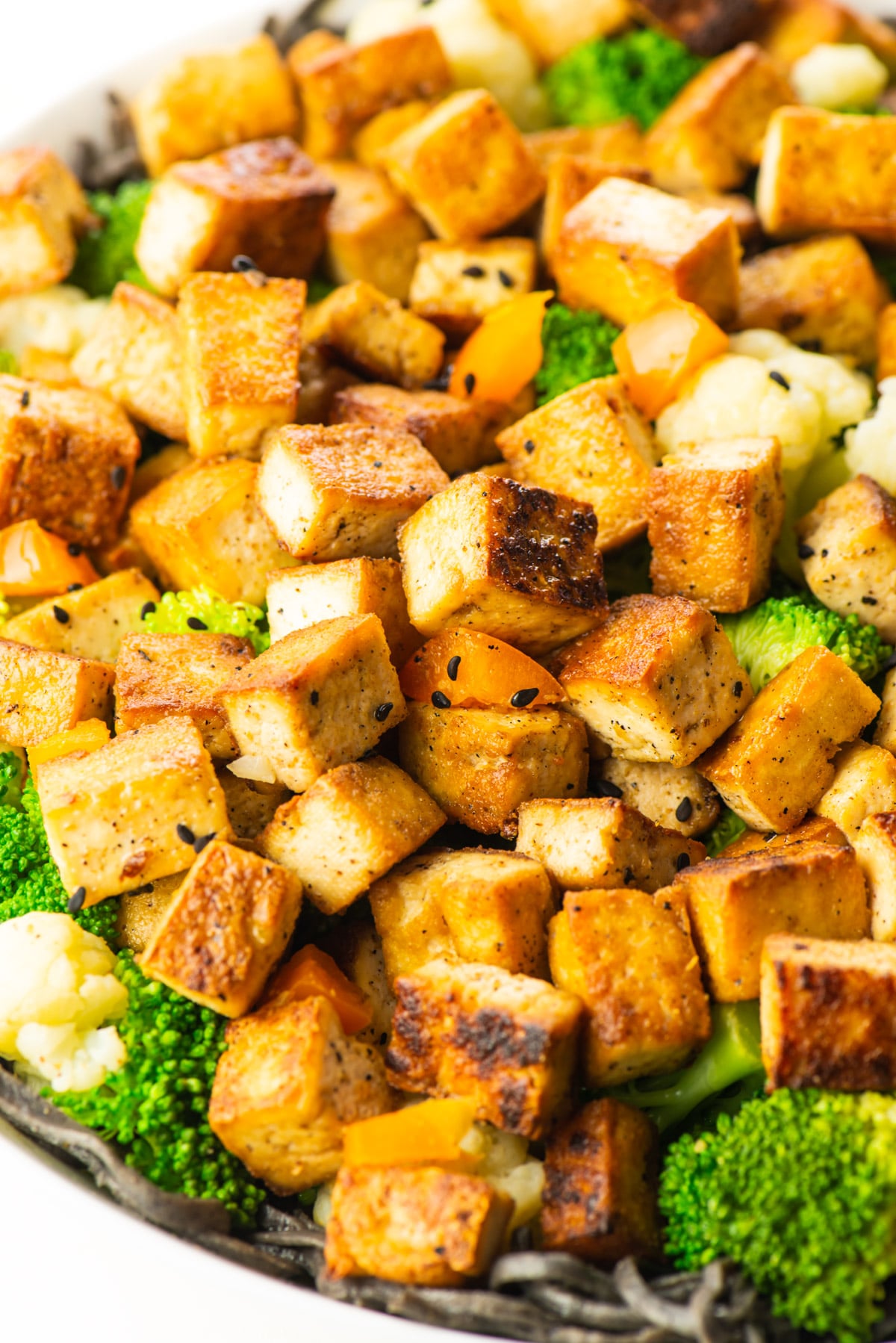 A closeup of tofu over noodles with steamed broccoli.