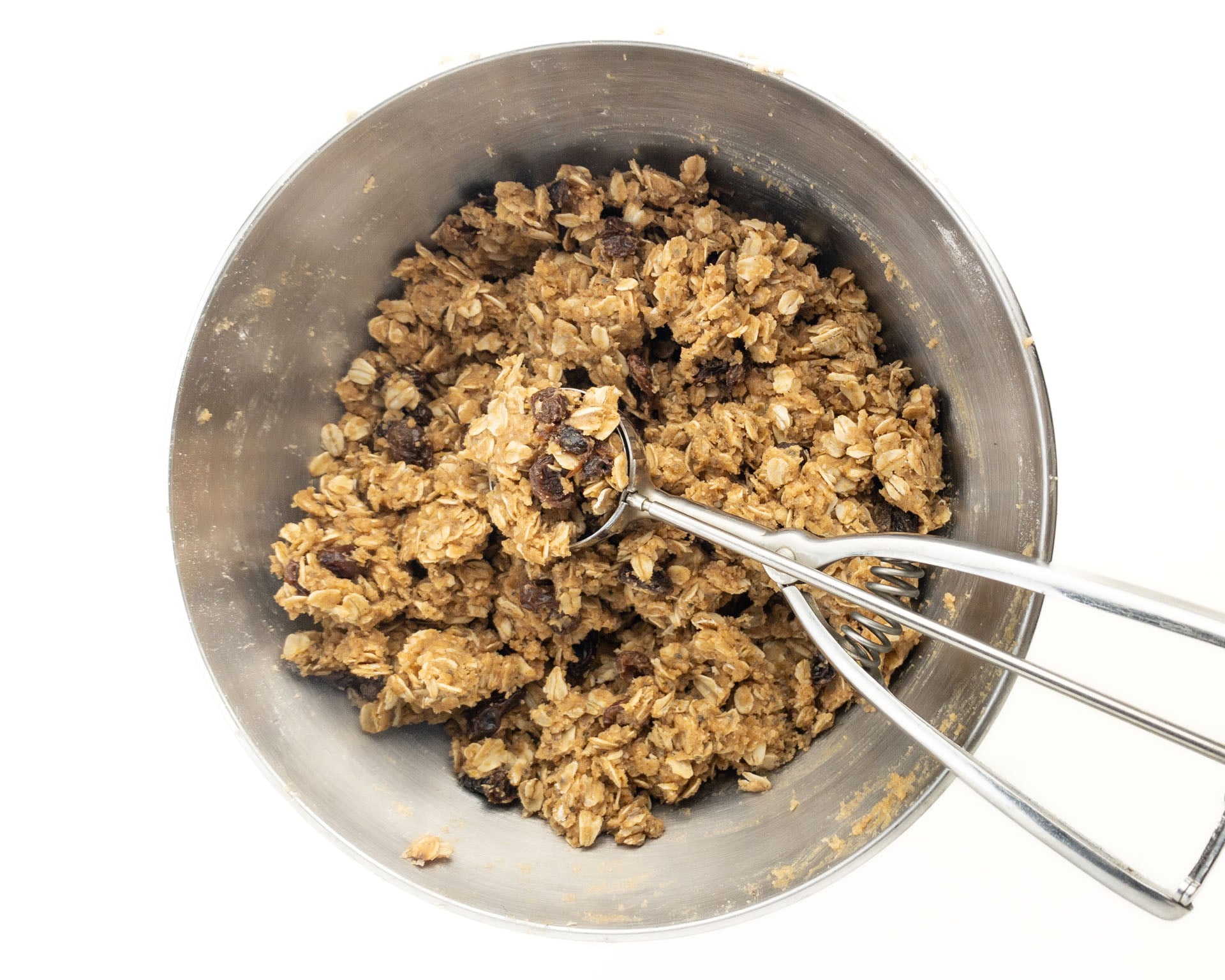 A mixing bowl holds oatmeal cookie dough with a cookie dough scoop in it.