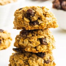 Three oatmeal cookies stacked with more cookies and ingredients around it.