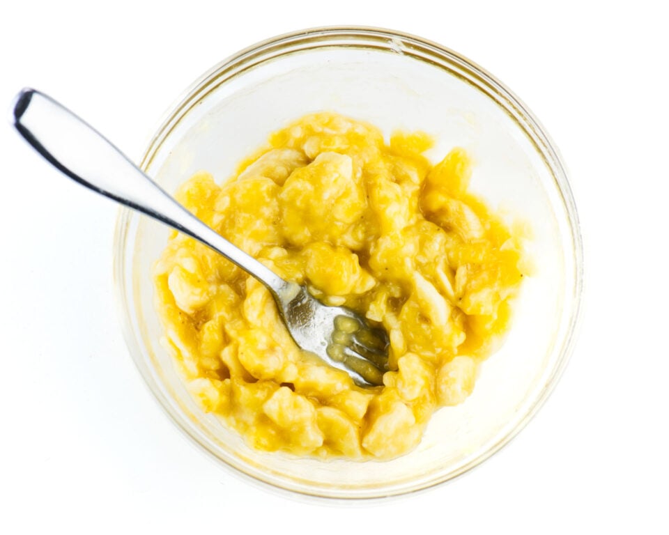 Mashed bananas in a glass bowl with a fork.