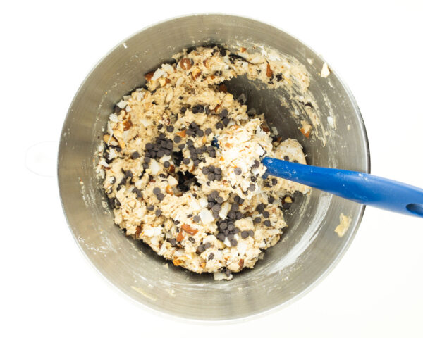 Cookie dough in a metal mixing bowl with a blue spatula.