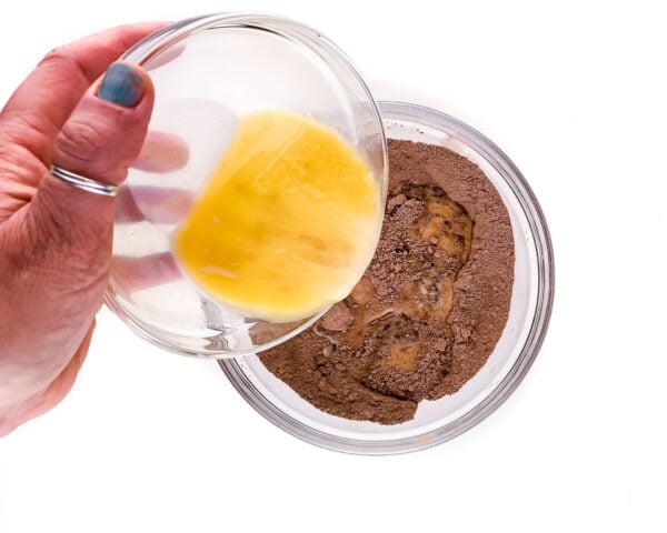 A hand pours melted butter over a cocoa powder base.