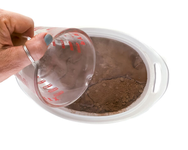 A hand pours hot water over chocolate cake batter.