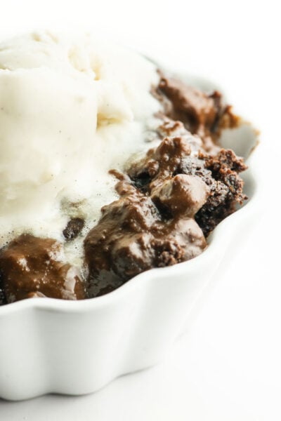 A closeup image of chocolate cake in a bowl topped with vanilla ice cream.
