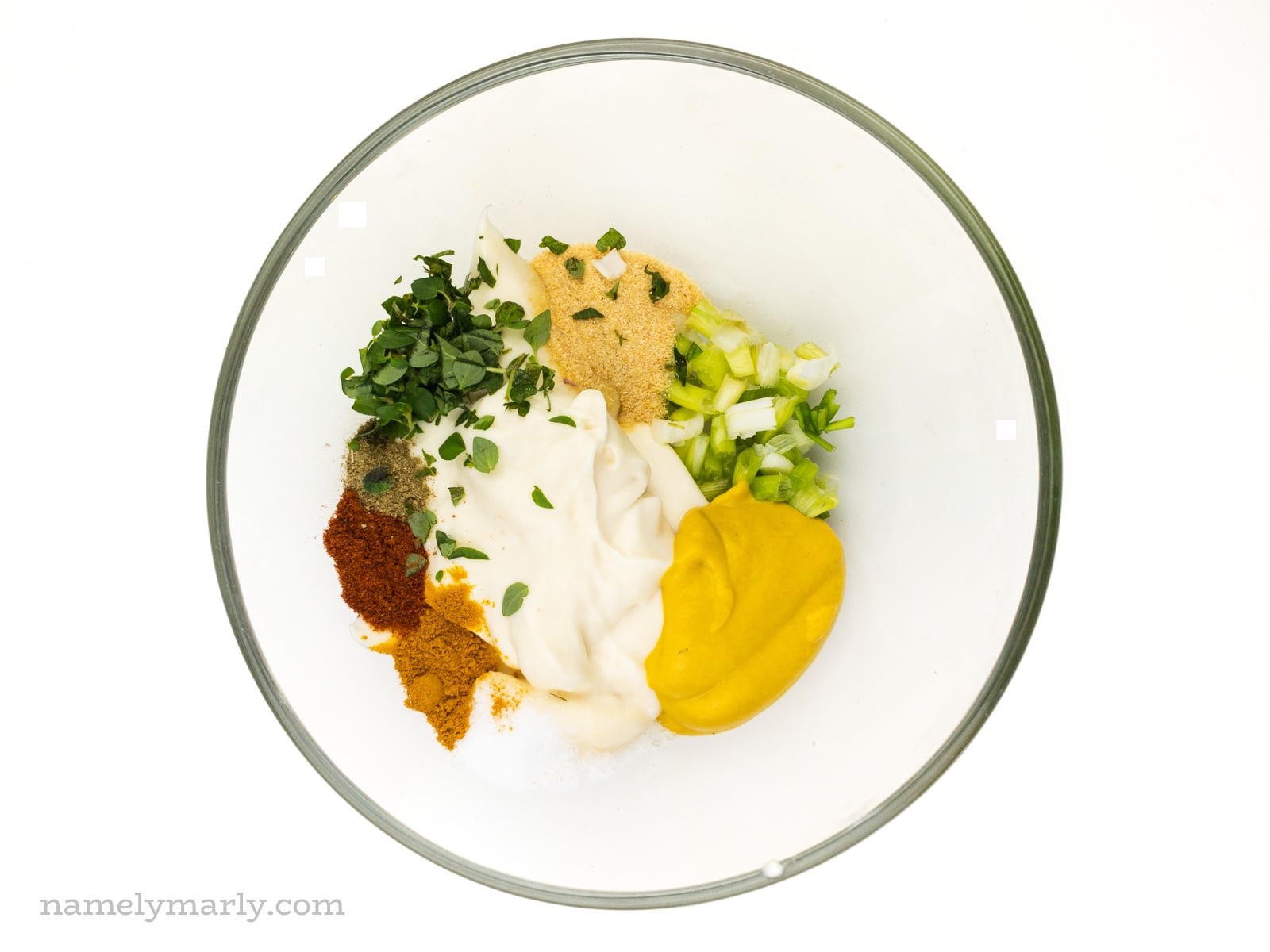 Ingredients like mustard, chopped green onions, vegan mayo, and other spices in a glass bowl.