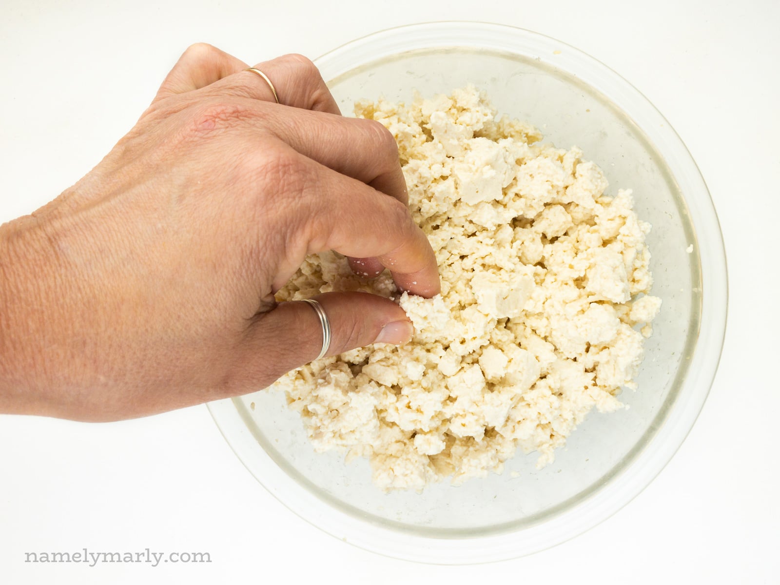 A hand reaches in a bowl of tofu, crumbling it up.