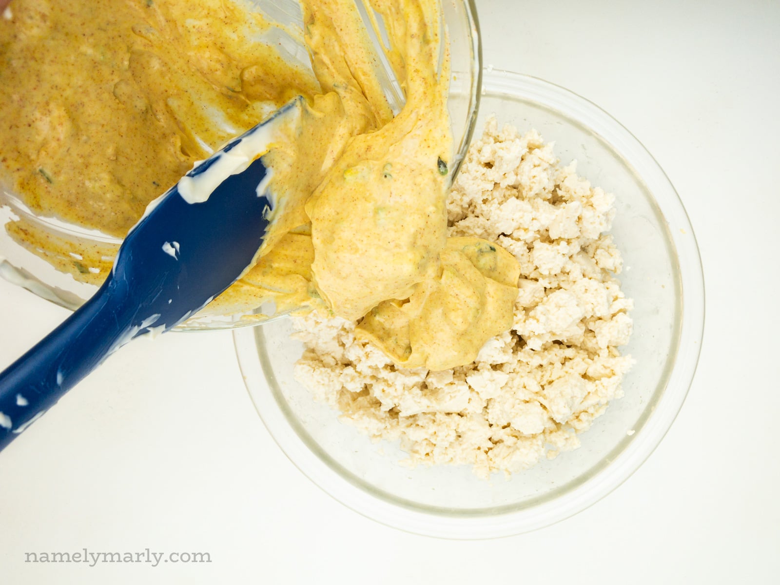 A bowl of yellow mustard sauce is being poured over a bowl of crumbled tofu.