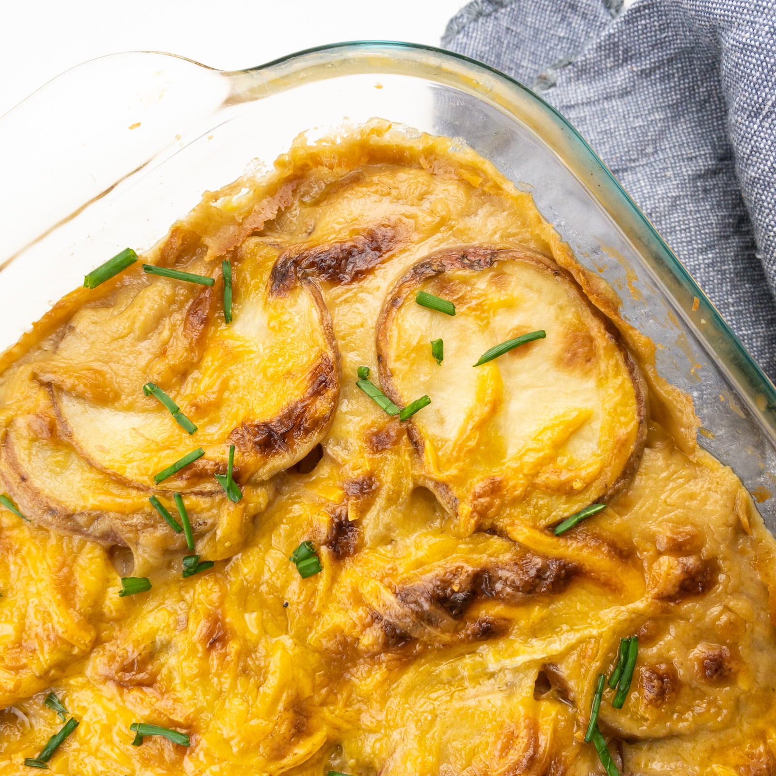 Looking down on a casserole dish full of vegan scalloped potatoes sitting on a grey kitchen towel. 