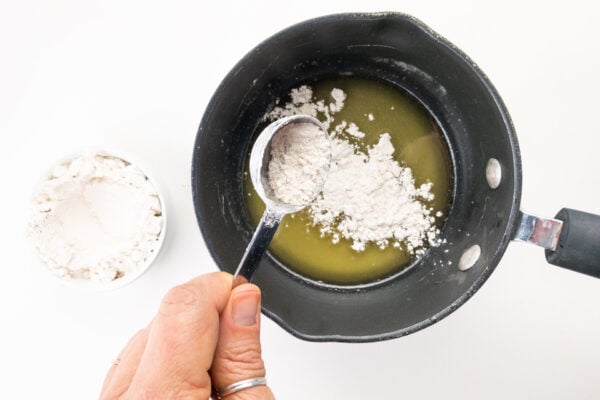 A hand pours flour over melted vegan butter in a sauce pan.