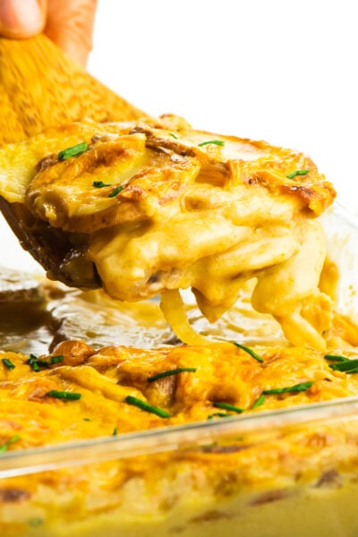 A hand holds a wooden spatula full of cheesy potatoes.
