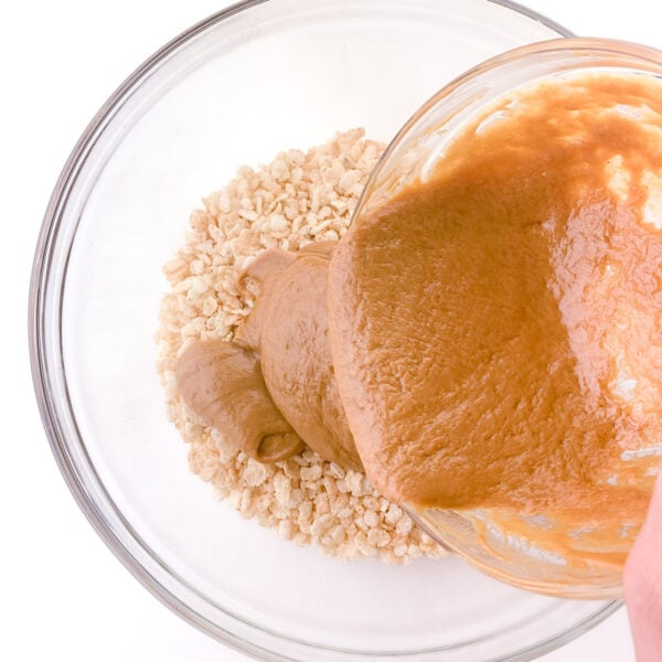 Peanut butter sauce is being poured over a bowl of rice krispies cereal.