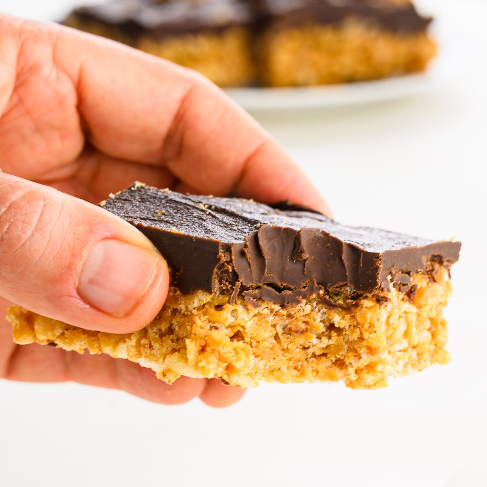 A hand holds a peanut butter rice krispies treat with a bite taken out of it.