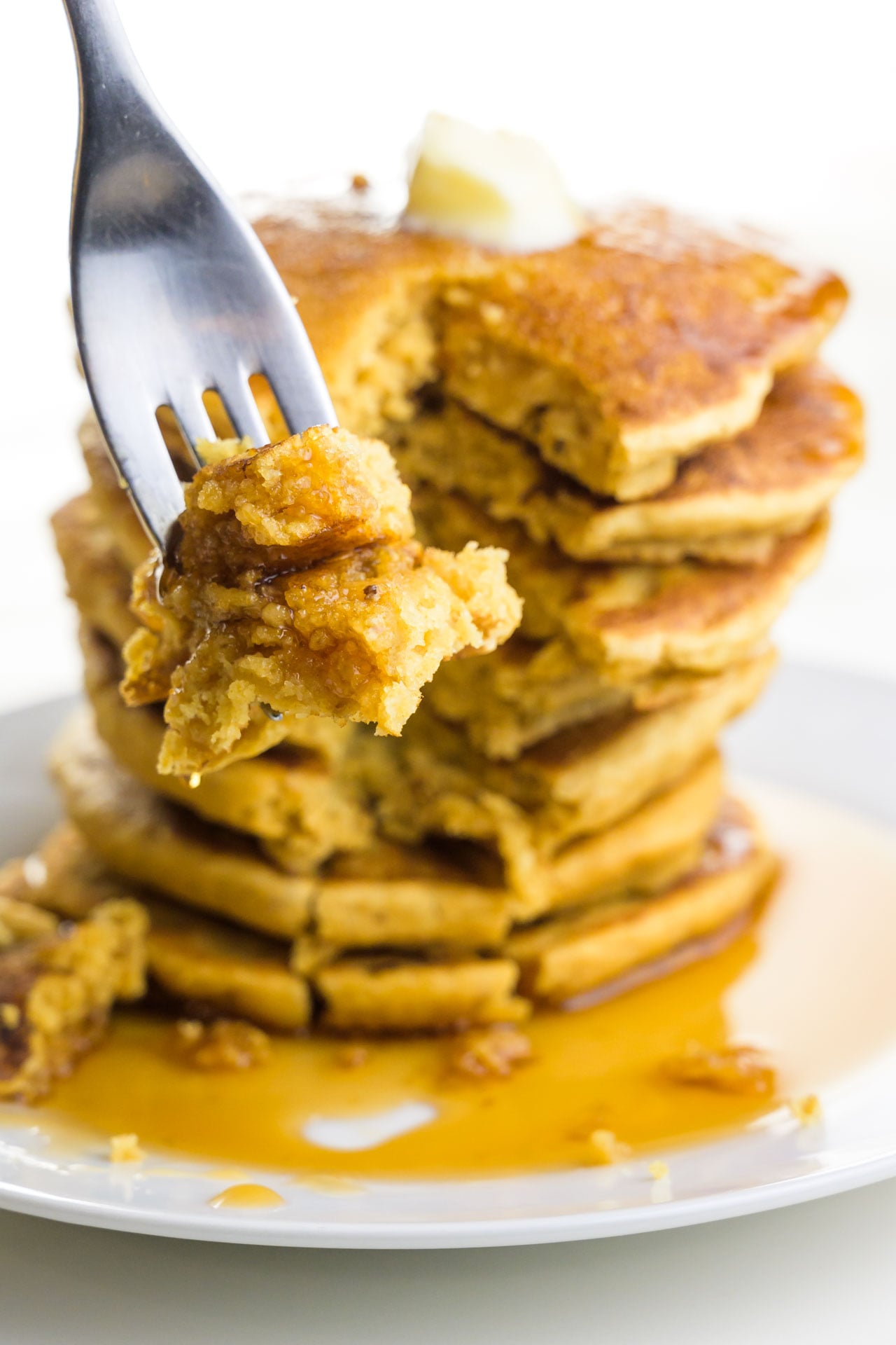 A fork holds a bite of pancakes in front of the rest of the plateful.