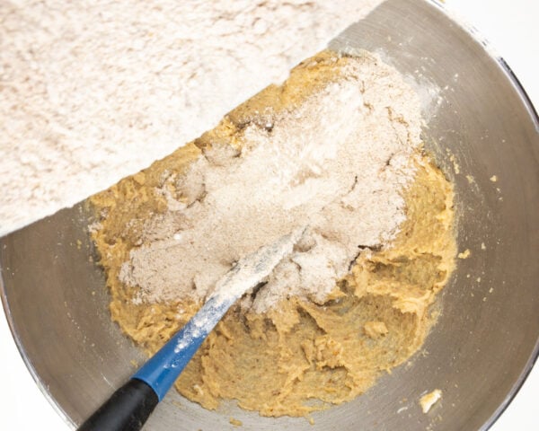 The dry ingredients are being poured into a mixing bowl with the butter sugar mixture.