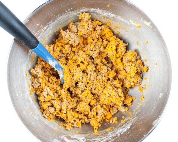 Cookie dough batter in the bottom of a mixing bowl with a spatula for stirring it.