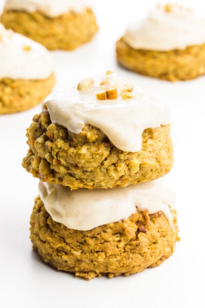 A stack of frosted carrot cake cookies sits in front of more cookies.