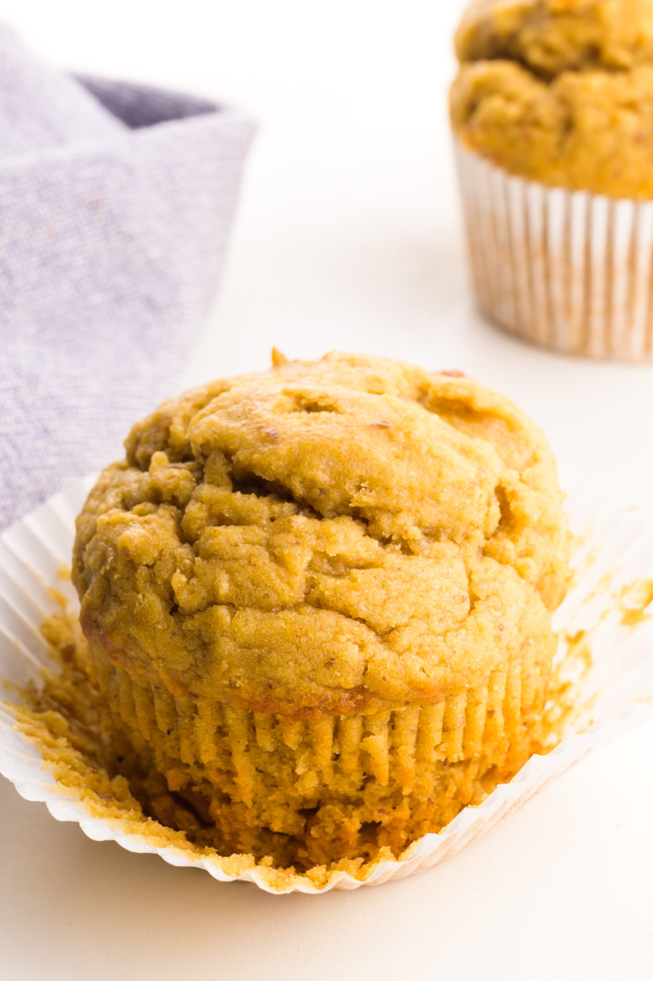 A muffin has a napkin behind it with another muffin behind it too.