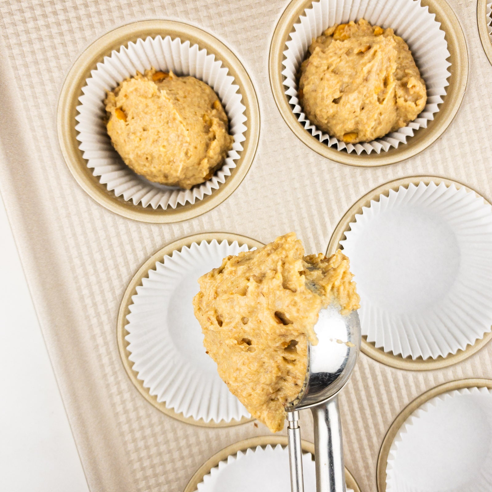 A cookie scooper is being used to add muffin dough into a muffin pan lined with papers.