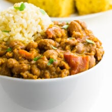 A bowl of red beans and rice is in the foreground with a plate of cornbread behind it.