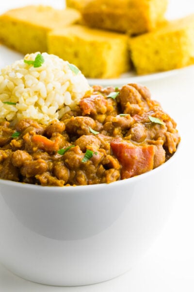 A bowl of red beans and rice is in the foreground with a plate of cornbread behind it.