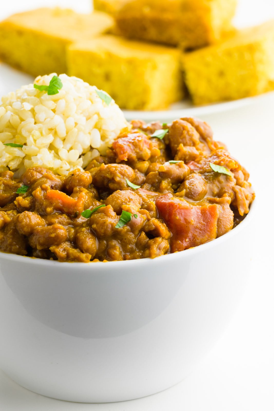 A bowl of red beans and rice is in the foreground with a plate of cornbread behind it.