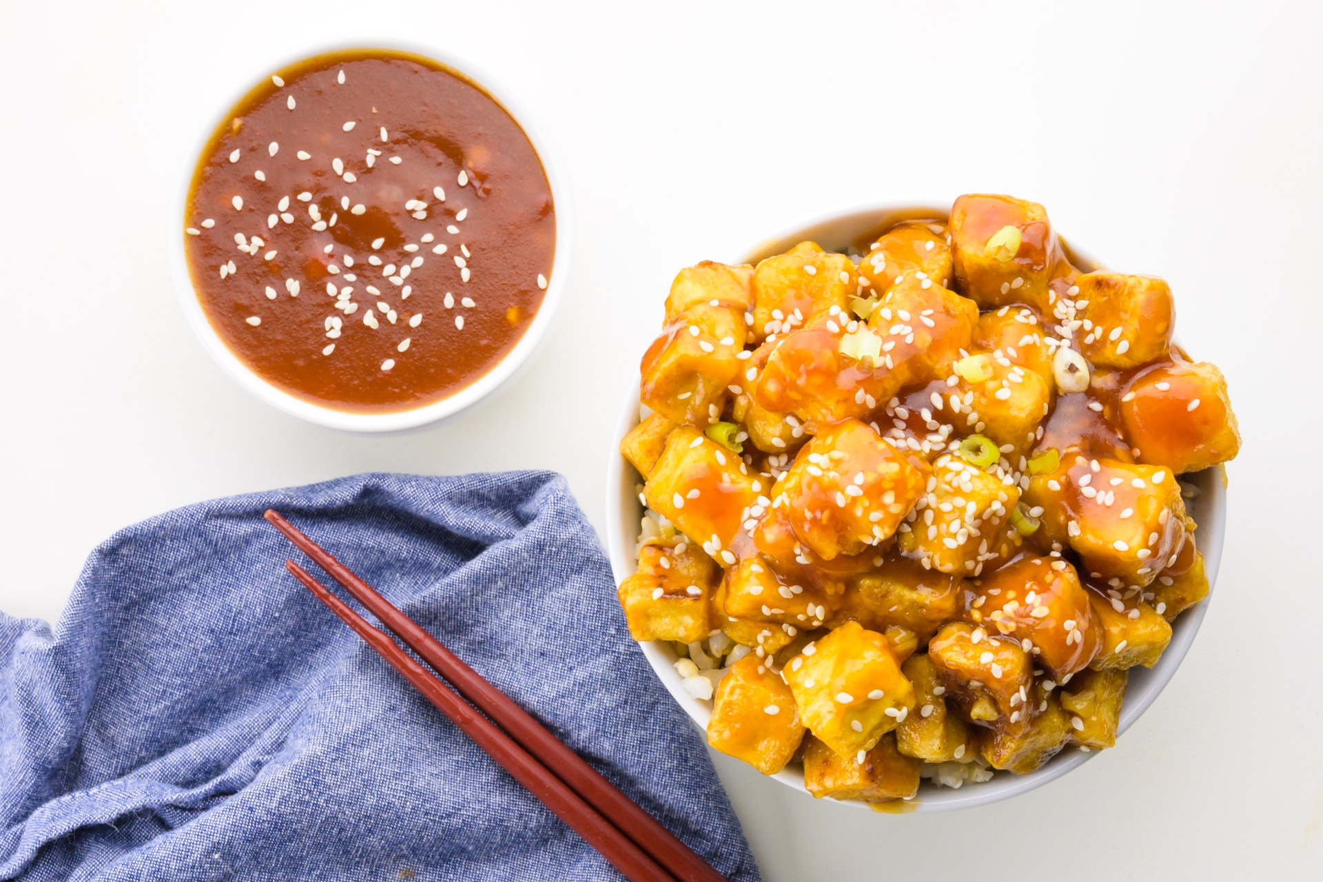 Looking down on a bowl of tofu sitting next to sauce and chopsticks.
