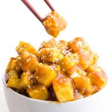 A chopstick holds a single bite over a bowl of sesame tofu.