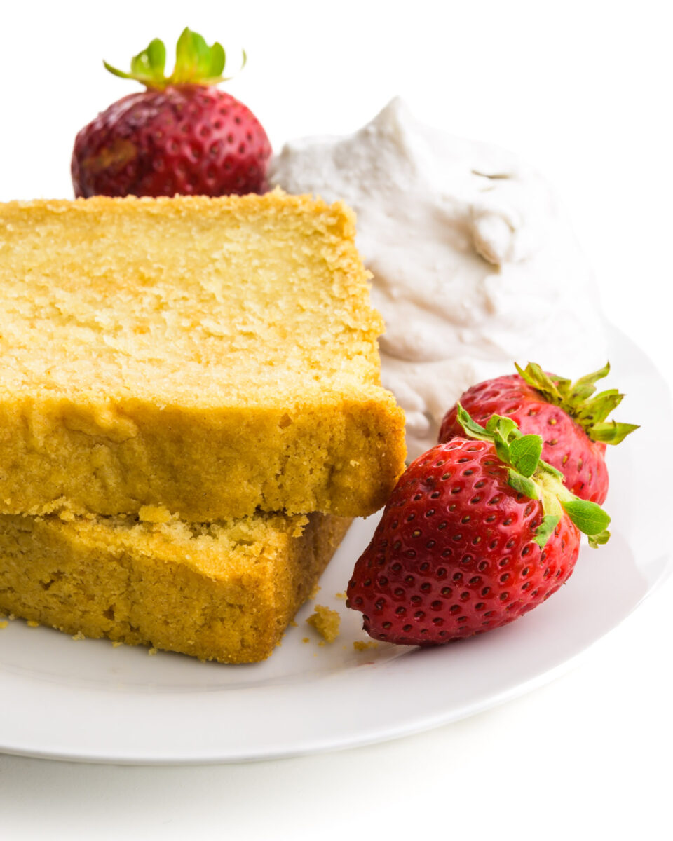 Two slices of pound cake are on a plate with strawberries and whipped cream.