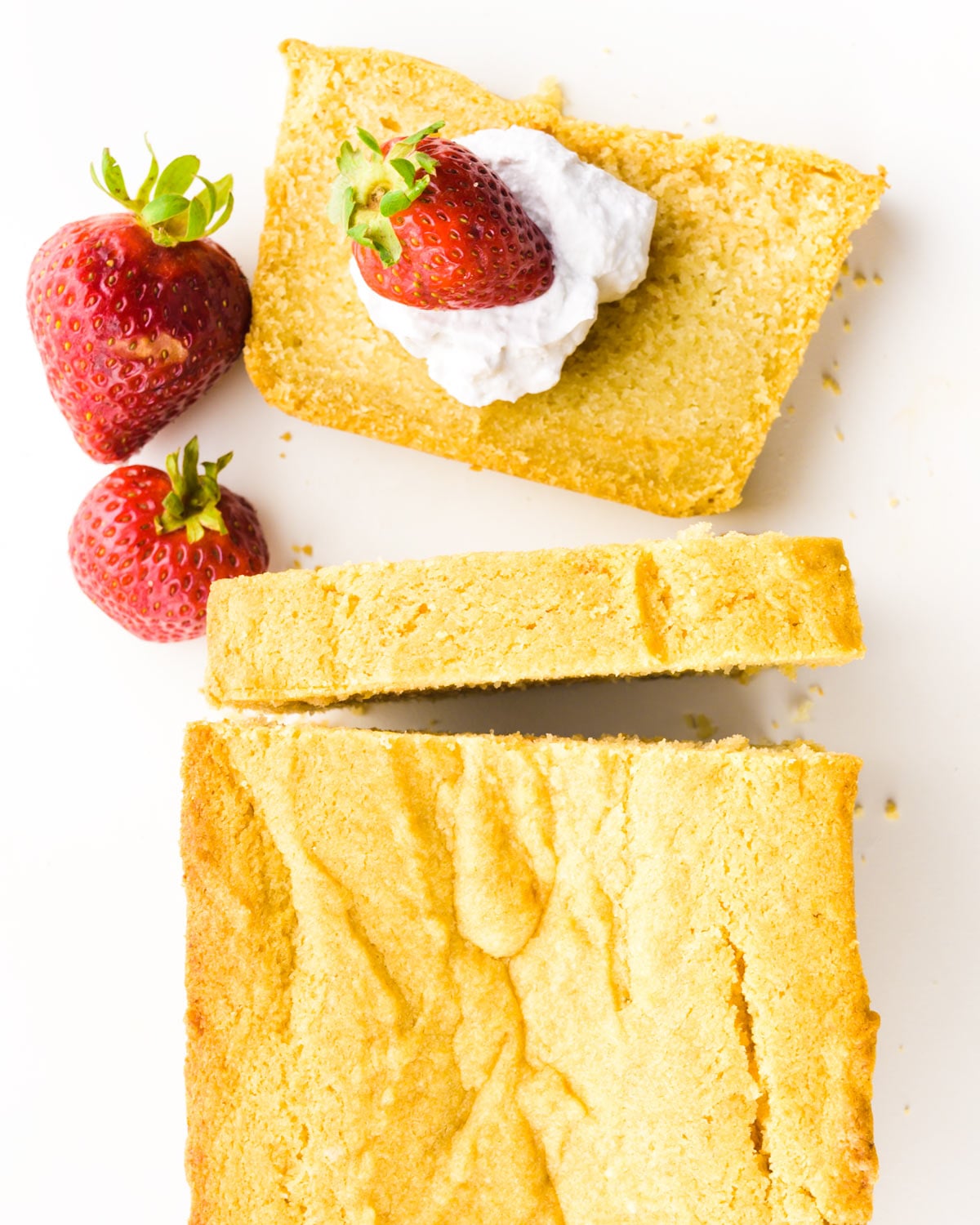 A slice of poundcake has whipped cream and strawberries on it with the rest of the pound cake loaf beside it.