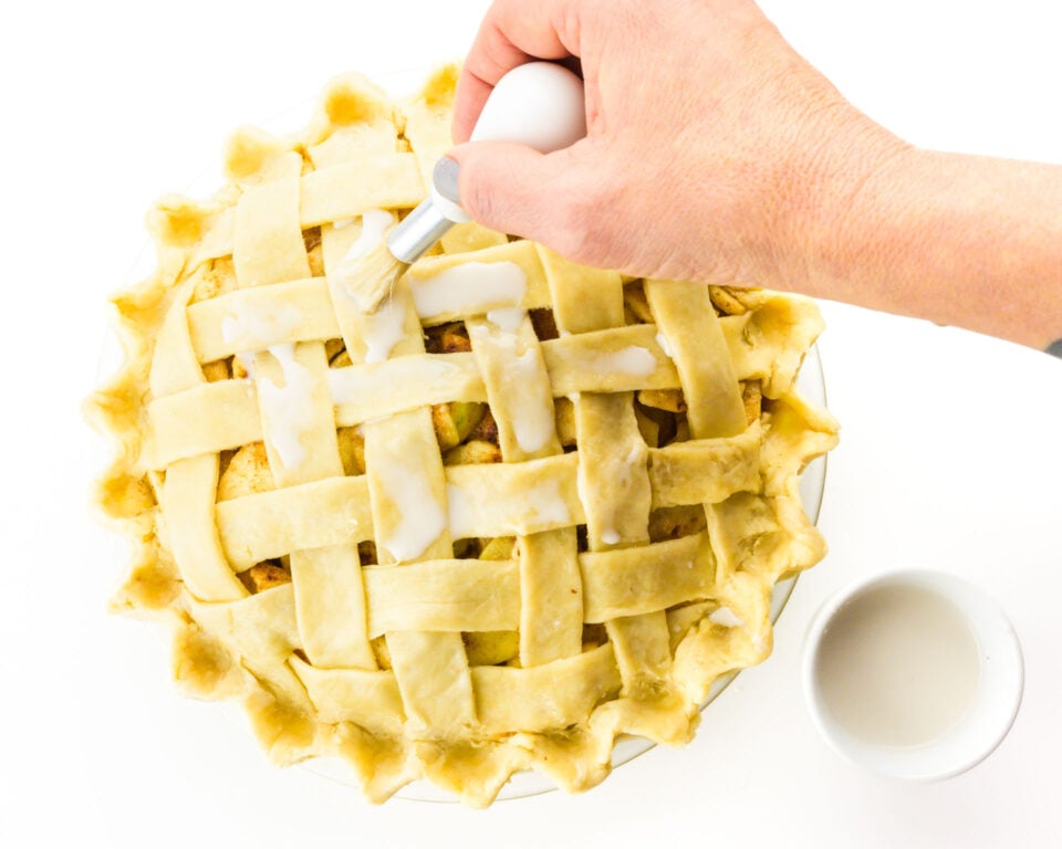 A hand holds a brush, adding vegan egg was to the unbaked pie crust.