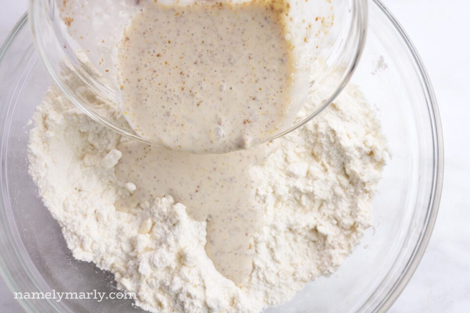 A creamy liquid is being poured into a bowl full of flour.