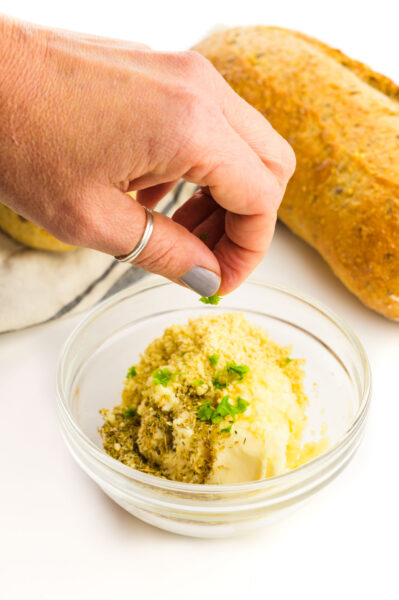 A hand sprinkles parsley over vegan garlic butter.