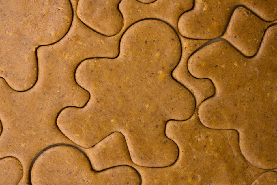 Gingerbread dough has been rolled and a cookie cut has been used to cut the shapes of gingerbread people in the dough.