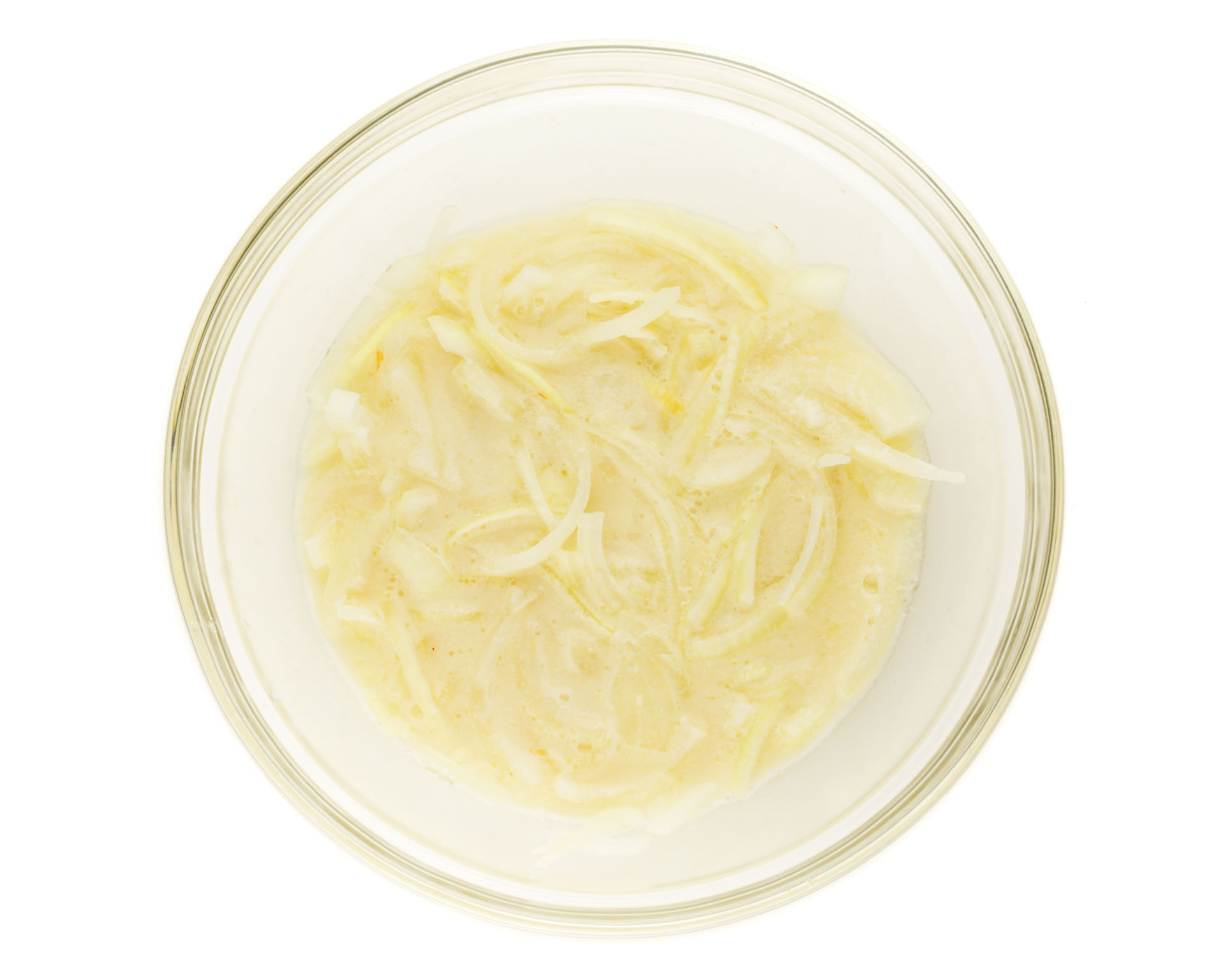 A bowl holds sliced onions are marinating in vegan buttermilk.