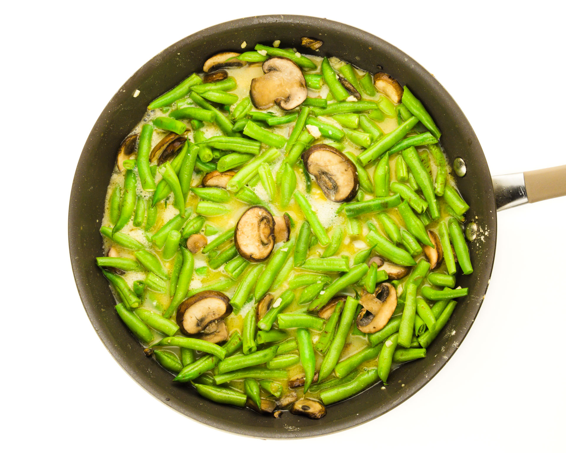 A skillet is full of green beans and mushrooms cooking.