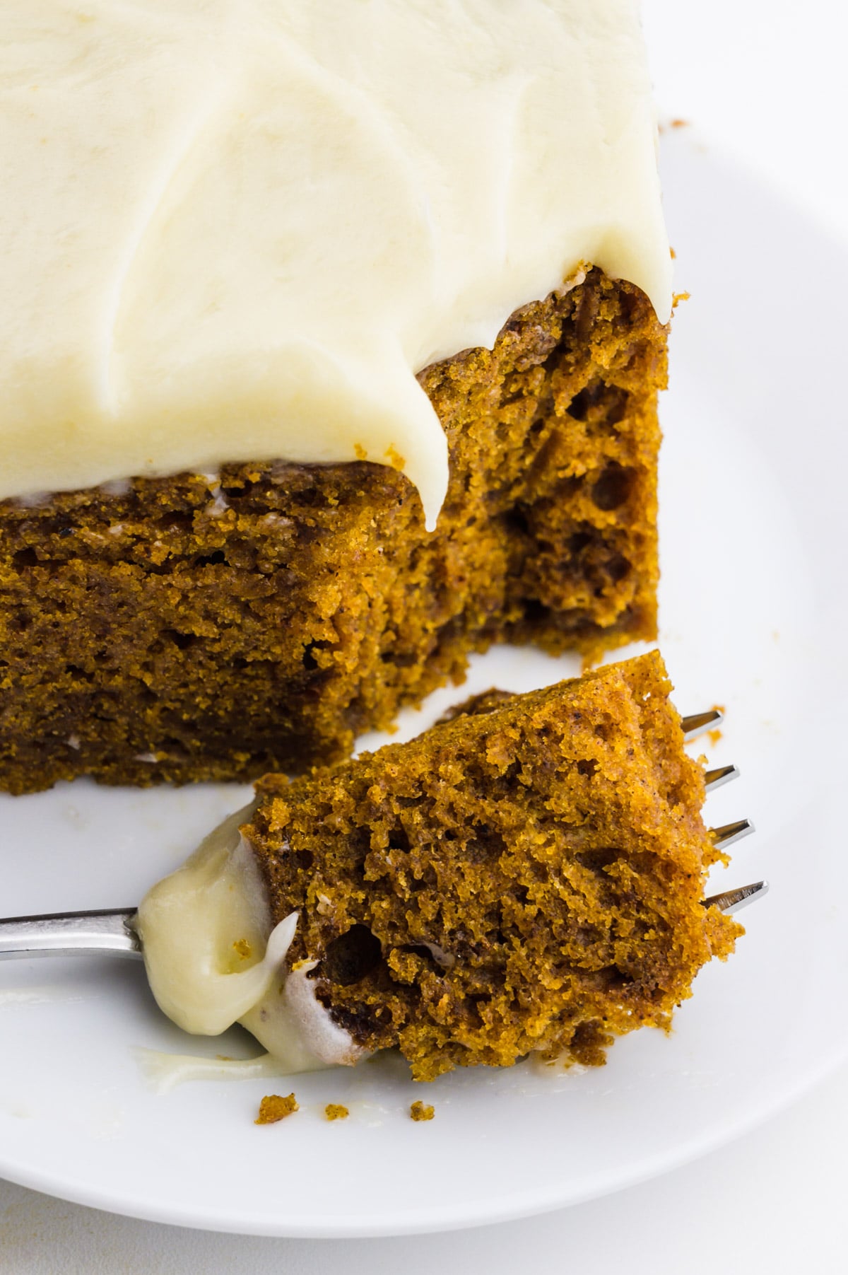 A close-up of a slice of cake with a fork holding one bite in front of the cake.