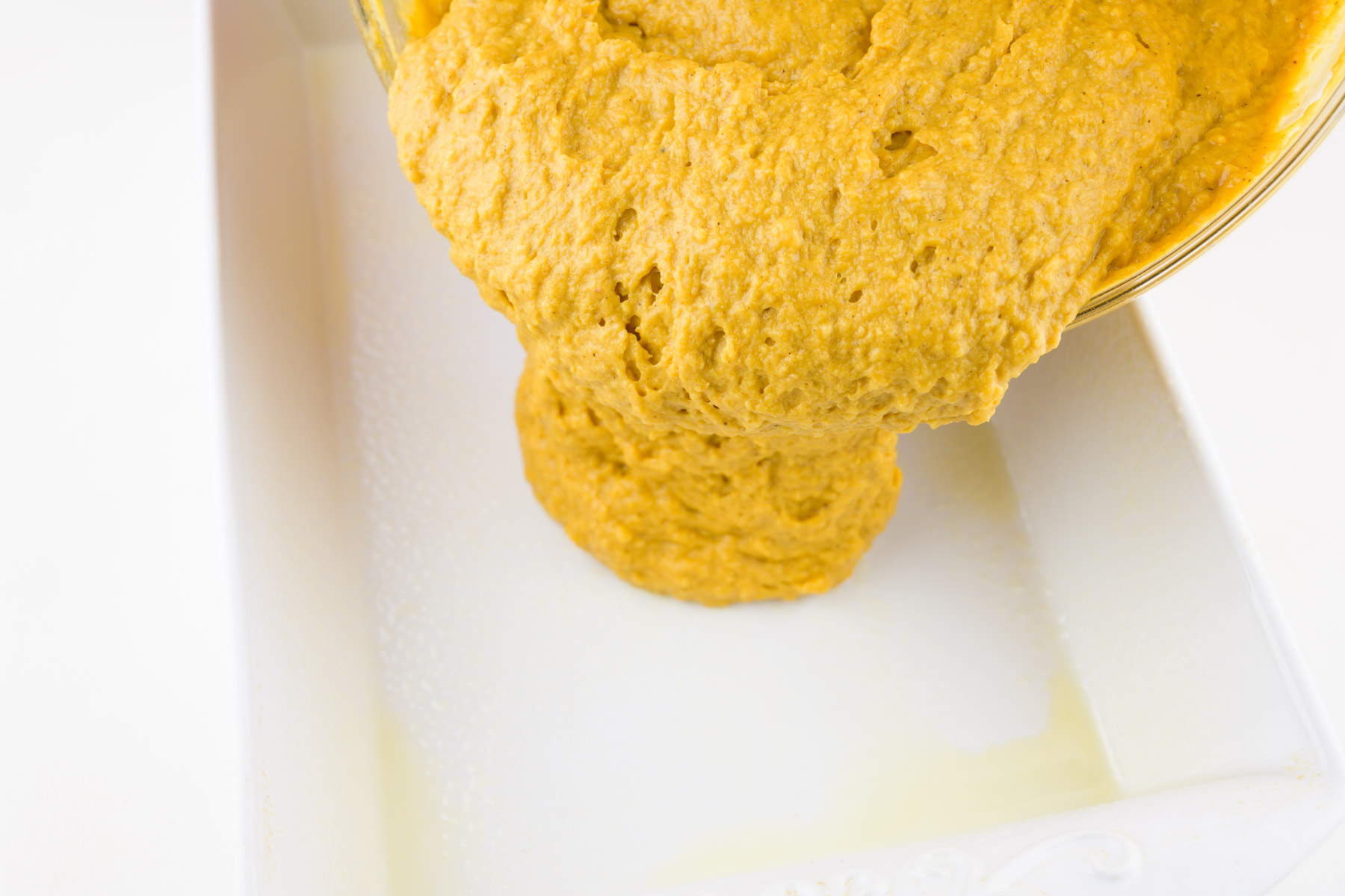 Cake batter is being poured into a white rectangle cake pan.